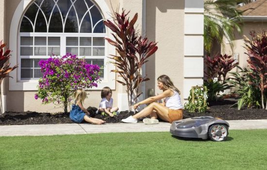 robotic lawn mower in a front yard with mom and 2 children planting a garden